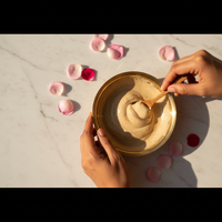 Hands holding golden bowl of Chandan cream with rose petals